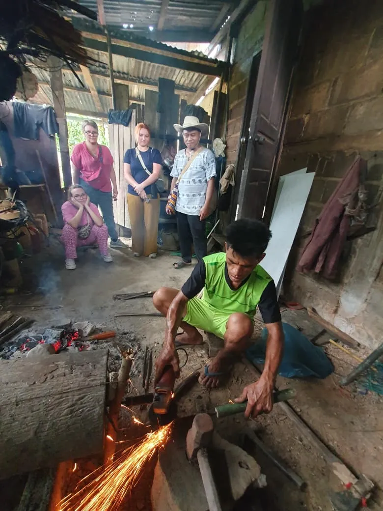 Khmu blacksmith forging a tool, sparks flying