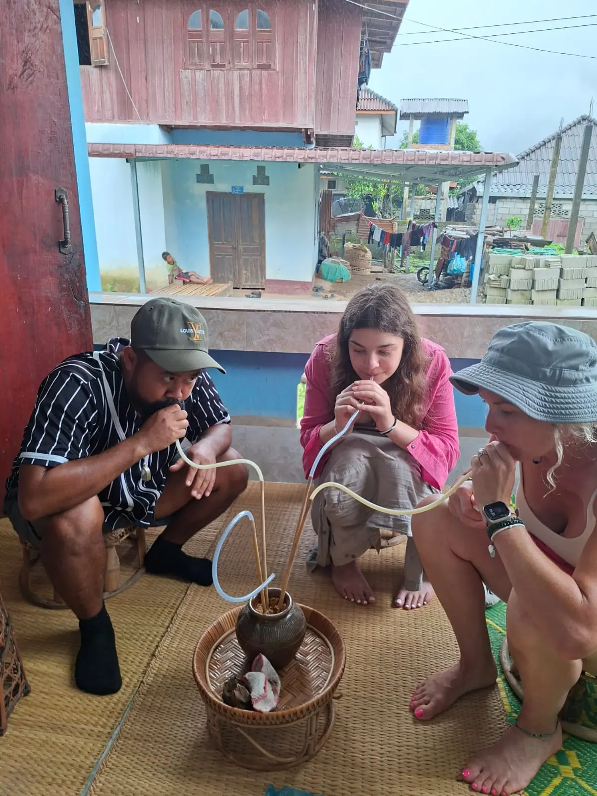 Travelers tasting traditional Khmu rice wine from a jar with straws